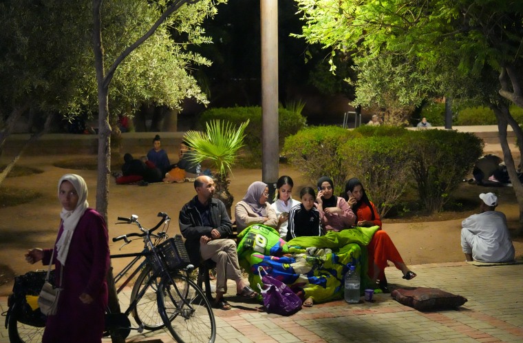 People sit under a blanket on a bench in a park after being made homeless by an earthquake on Sept. 9, 2023 in Marrakech, Morocco. 