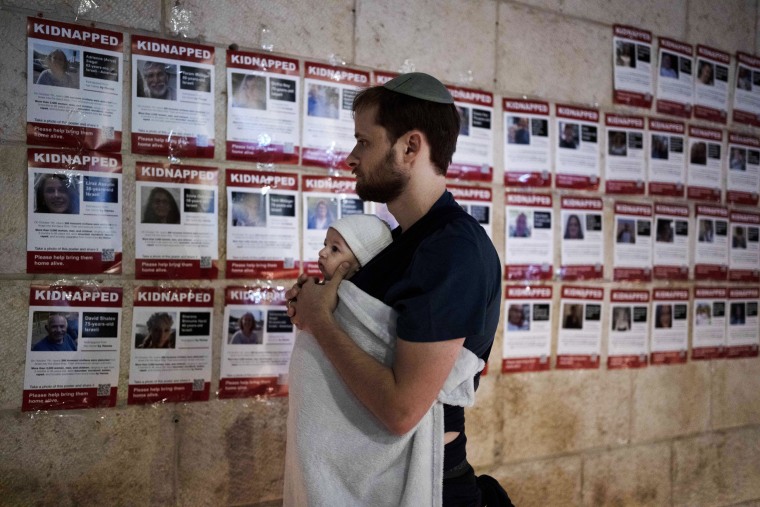 A man holds his baby as he looks at posters of the men, women and children held hostage by Hamas in the Gaza Strip during a vigil in Jerusalem on Nov. 5, 2023.